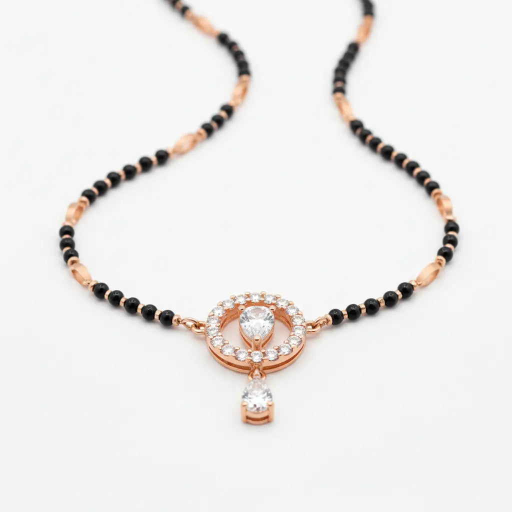 A black and rose gold beaded necklace with a central circular pendant featuring a heart-shaped clear gemstone and a dangling clear stone, set against a plain white background.