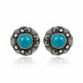 A pair of round sterling silver stud earrings featuring a central round turquoise cabochon stone surrounded by textured silver details and small raised silver beads, set against a plain white background with a soft reflection below.