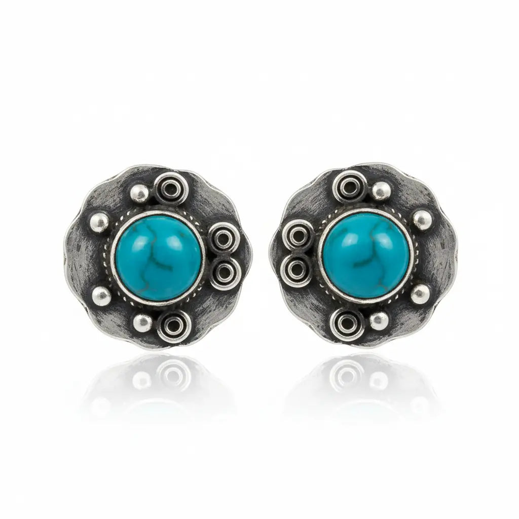 A pair of round sterling silver stud earrings featuring a central round turquoise cabochon stone surrounded by textured silver details and small raised silver beads, set against a plain white background with a soft reflection below.