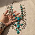 Turquoise and silver necklace held by a hand on a beige background