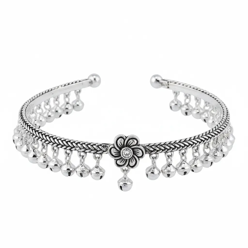 A silver-toned metal cuff bracelet featuring a braided pattern, dangling bell charms, and a central flower motif with a small clear stone, shown on a plain white background.