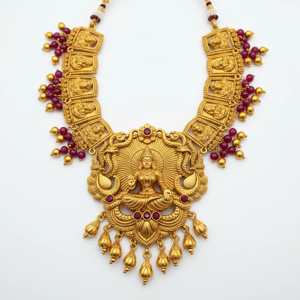Gold necklace with intricate design and red stones on a white background